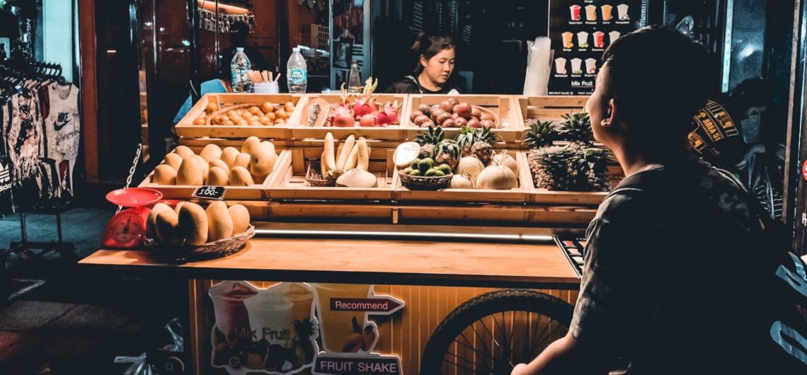 Puesto callejero en Bangkok con de diferentes tipo de fruta y un cliente esperando ser atendido