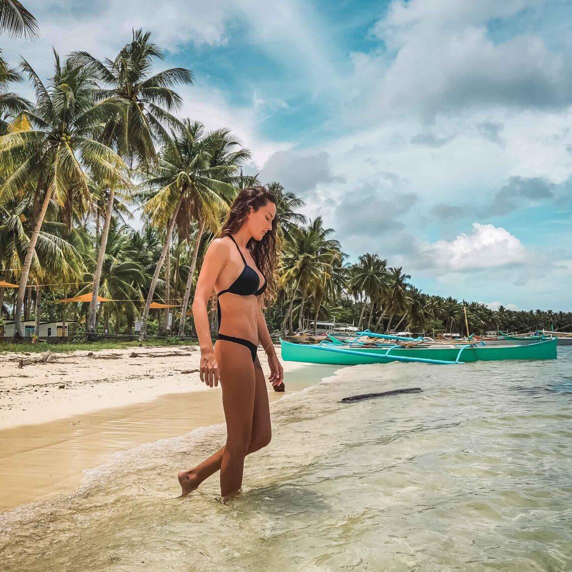 Mujer caminando por una playa tropical con palmeras y barcas tradicionales